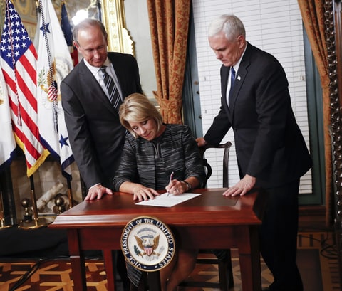 Vice President Mike Pence, right, watches as newly sworn in Education Secretary Betsy DeVos, center, signs the affidavit of appointment in the Eisenhower Executive Office Building in the White House complex in Washington, Tuesday, Feb. 7, 2016, as DeVos' husband Dick DeVos, right, watches.