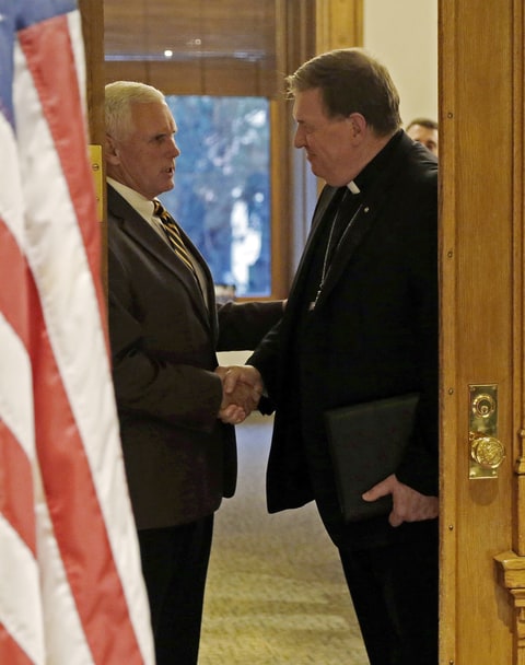 Indianapolis Archbishop Joseph Tobin, right, shakes hands with Indiana Gov. Mike Pence following a meeting at the Statehouse Wednesday, Dec. 2, 2015, in Indianapolis, the day after the archdiocese said it has the means to resettle a Syrian refugee family bound for the state. Pence blocked state agencies from distributing federal money for Syrian refugees following the deadly Paris attacks.