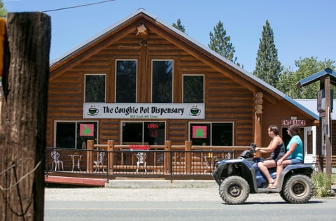 Tourists on a four-wheel leisure vehicle pass the Coughie Pot marijuana dispensary July 2, 2017 as they visit the small historical gold mining town of Sumpter, Oregon. City leaders had a chance to opt out of having recreational marijuana stores within their area until the end of 2015, per state rules. But around that time, councilors were wrapped up in other issues and basically forgot to opt out.