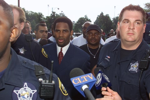 Grammy-winning singer R. Kelly (C) is surrounded by sheriff's deputies and the media as he is escorted into Cook County Circuit Court in Chicago, Illinois June 25, 2002. Kelly pleaded innocent to 21 counts of child pornography.
