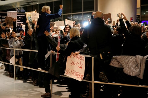 Sen. Elizabeth Warren of Massachusetts stands on a railing to address demonstrators at Logan Airport in January.